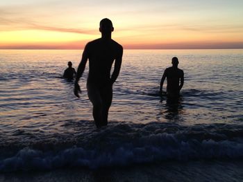 Silhouette people on beach against sky during sunset