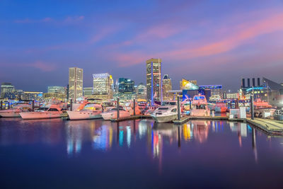 Boats moored in river against illuminated buildings in city