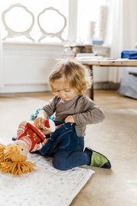 Cute baby girl playing with toys while sitting on floor at home