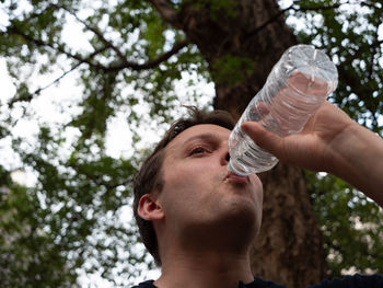 Low angle view of man drinking glass against trees