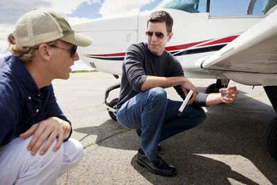 Men crouching while working by airplane at hangar