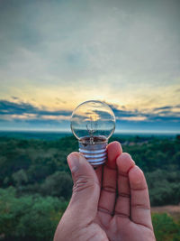 Person hand holding glass of water against sky