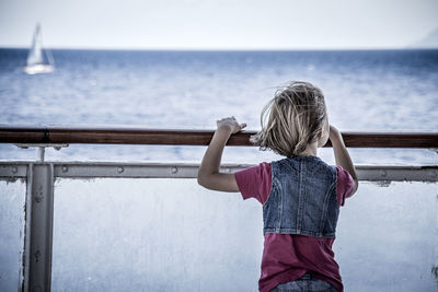 Rear view of girl standing by sea against clear sky