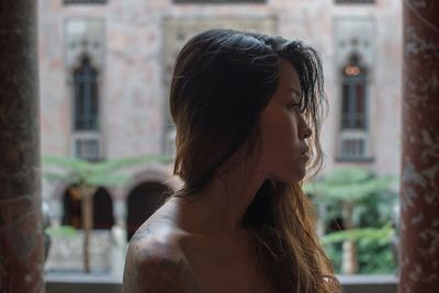 Rear view of shirtless young woman standing by window