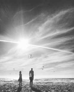 Rear view of man and woman standing at beach against sky on sunny day