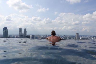 Rear view of shirtless man in swimming pool against sky