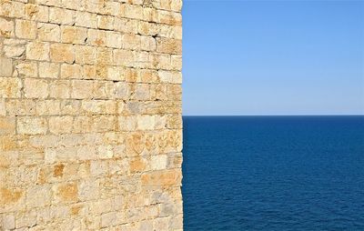 Brick wall by sea against clear blue sky