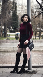 Young woman looking away standing against pole in city