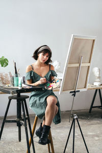 Portrait of young woman painting on canvas while sitting on table