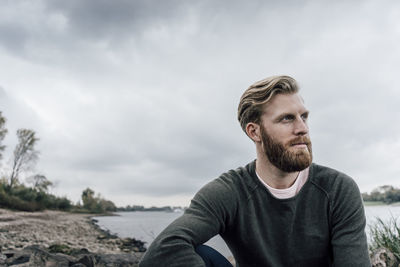 Young man sitting at the river in autumn, portrait