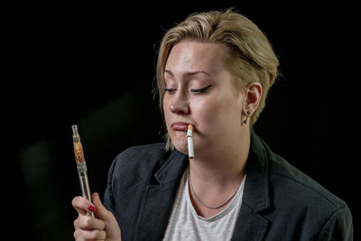 Close-up of young woman smoking over black background