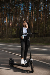 Woman talking over smart phone while standing on road against trees