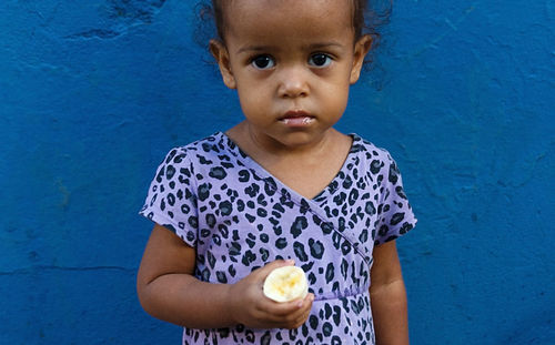 Portrait of girl holding food standing against blue wall