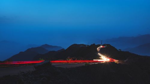 Light trails on mountain against sky at night