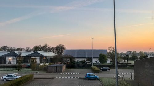 Cars on street by buildings against sky during sunset