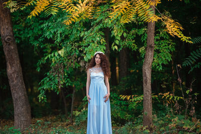 Portrait of woman standing by tree in forest