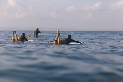 Friends surfing on sea against sky