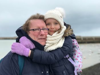 Close-up portrait of girl embracing grandfather against sea during winter