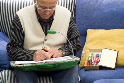 Senior man drawing on book while sitting on sofa at home