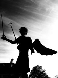 Low angle view of silhouette man holding statue against sky