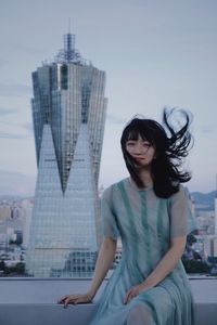 Portrait of woman sitting against modern building in city