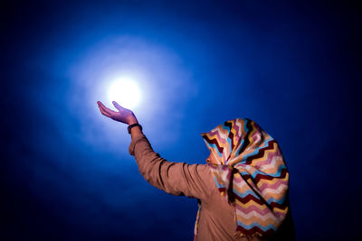 Optical illusion of woman holding glowing moon against sky at night
