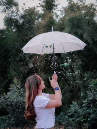 Woman holding umbrella while standing by plants during rainy season