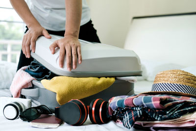 Midsection of woman packing overburdened clothes in suitcase 