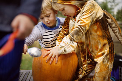 Brothers carving pumpkin at yard during halloween