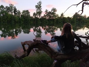 Rear view of woman sitting on lake against sky