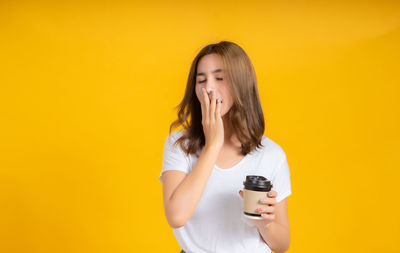 Young woman standing against yellow background