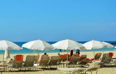 Chairs and parasols on beach against clear blue sky