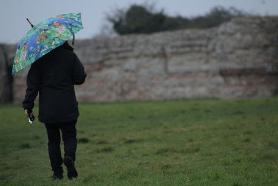 Rear view of woman walking on field during rainy season