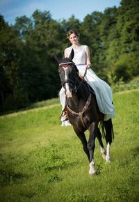 Young woman riding horse on grassy field