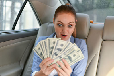 Surprised businesswoman looking at paper currency while sitting in car