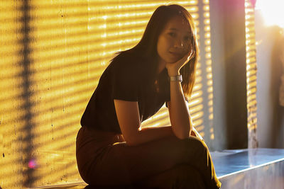 Portrait of young woman sitting in city during sunset