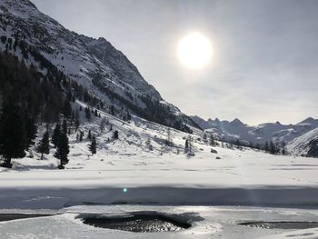 Scenic view of snow covered mountains against bright sun