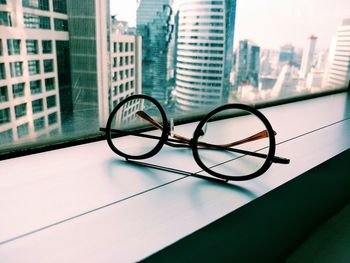 Close-up of eyeglasses on window sill against buildings in city