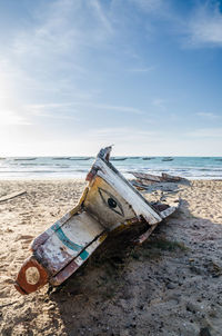 Abandoned boat on beach against sky