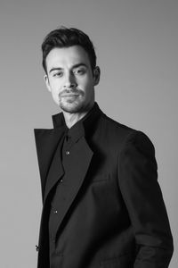 Portrait of handsome young man in suit standing against gray background