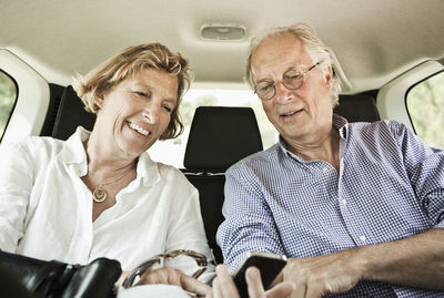 Happy couple looking in mobile phone while sitting in car