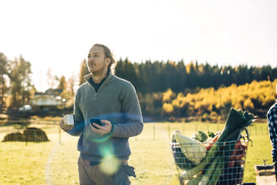 Thoughtful man holding coffee cup and mobile phone at farmer's market