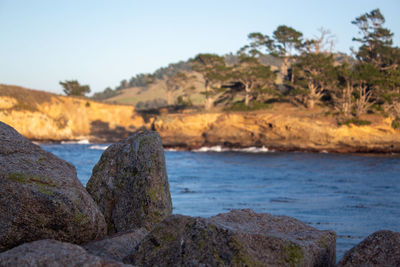 Scenic view of rocks by sea against clear sky