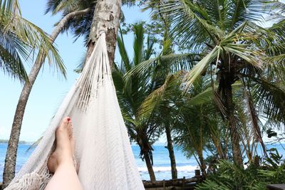 Low section of woman relaxing in hammock against sea at beach