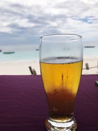 Close-up of beer in glass on table against sea