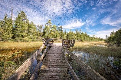 Old wooden jetty over swamp against sky