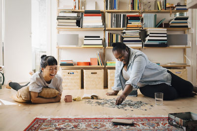 Happy female friends playing puzzle on floor at home