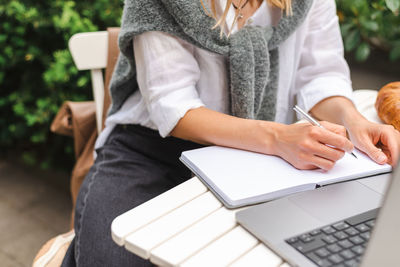 A woman takes notes in front of a laptop during a business meeting in a cafe.