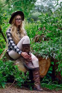 Young woman standing by plants against trees