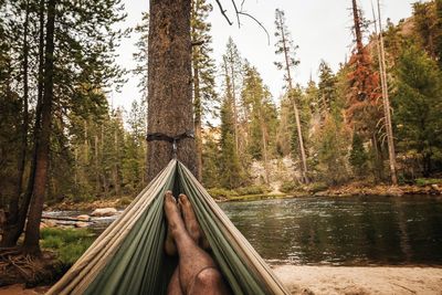 Low section of man lying on hammock at lake